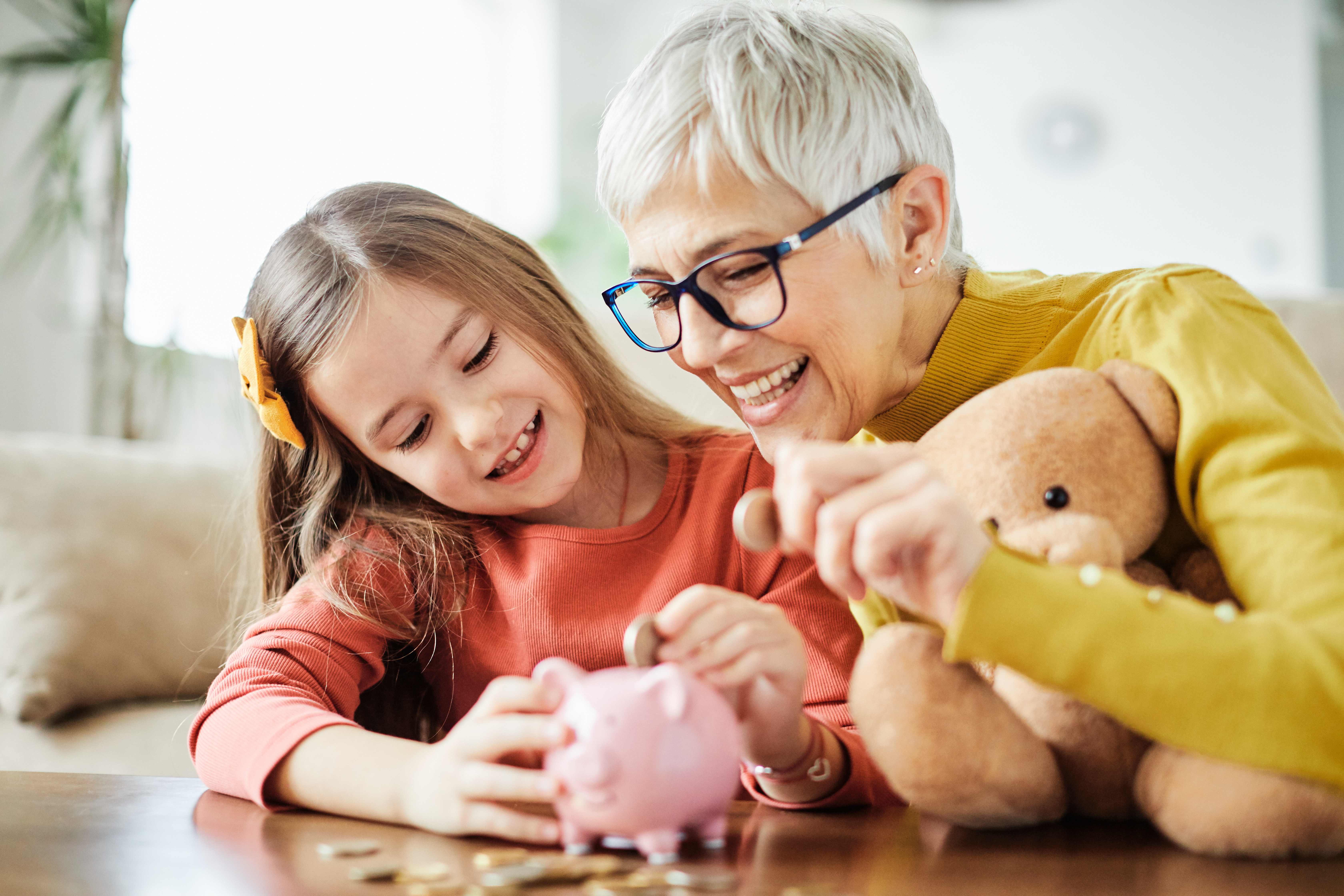 An older woman and a young child put coins into a piggy bank